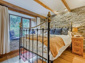 A bedroom with a stone wall, a metal bed frame, a wooden nightstand, and a window with curtains. - 3 Bed in Padstow (oc-51214) (Padstow)