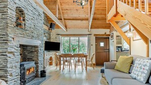 A cozy living room with a stone fireplace, wooden beams, a TV, and a sofa. - 3 Bed in Padstow (oc-51214) (Padstow)