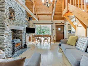 A cozy living room with a stone fireplace, wooden beams, a TV, and a sofa. - 3 Bed in Padstow (oc-51214) (Padstow)
