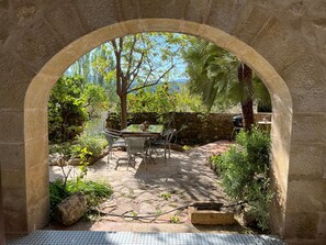 An outdoor patio with stone walls, a table with chairs, and a view of greenery and a mountain.