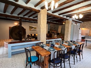 A rustic dining area with exposed wooden beams, stone pillars, and a large table set for a meal.