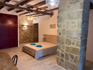 A bedroom with a stone wall, wooden ceiling beams, a bed with a wooden headboard, and a red door.