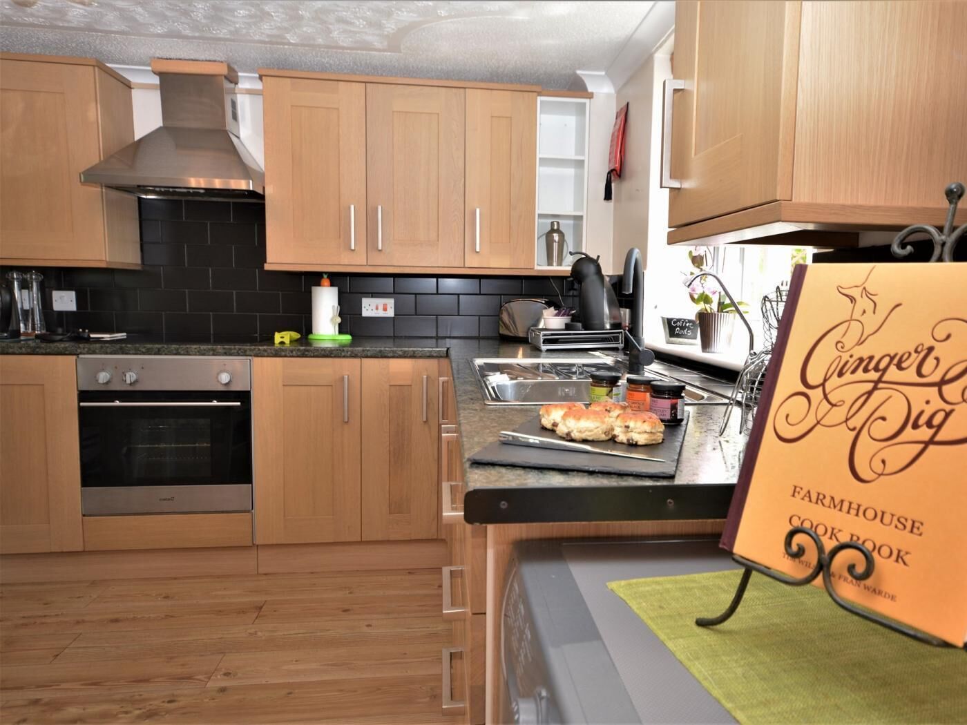 A kitchen with wooden cabinets, a stove, a coffee machine, and a cookbook on the counter.