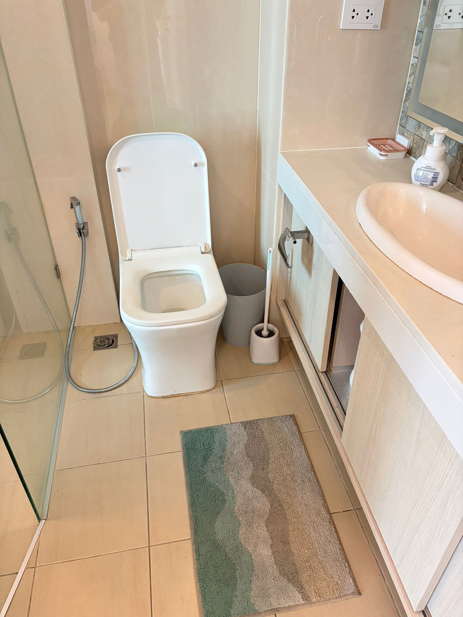 Une salle de bain comprenant des toilettes, un bidet, une douche, un lavabo et une petite poubelle.