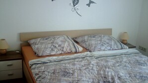 Een bed met beddengoed met patroon, twee nachtkastjes met lampen, en een muurdecoratie met vogels en bladeren.