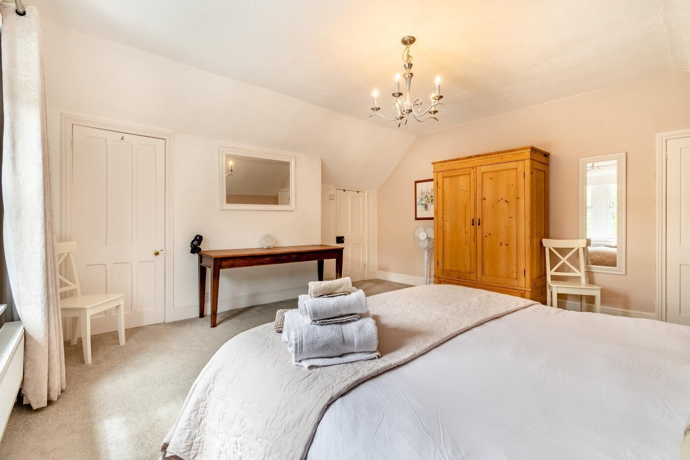 A bedroom with a bed, a wooden wardrobe, a desk, a chair, and a mirror.