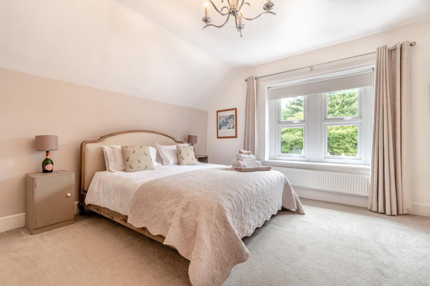A bedroom with a bed, a nightstand, a lamp, a window with curtains, and a radiator.