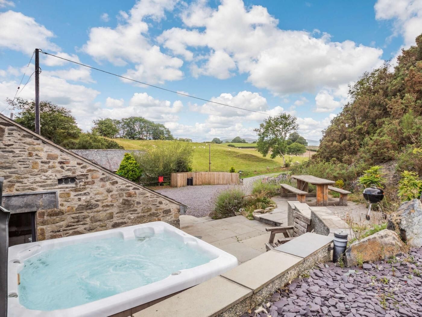 A stone building with a hot tub, outdoor seating, and a view of a grassy field.