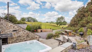A stone building with a hot tub, outdoor seating, and a view of a grassy field.