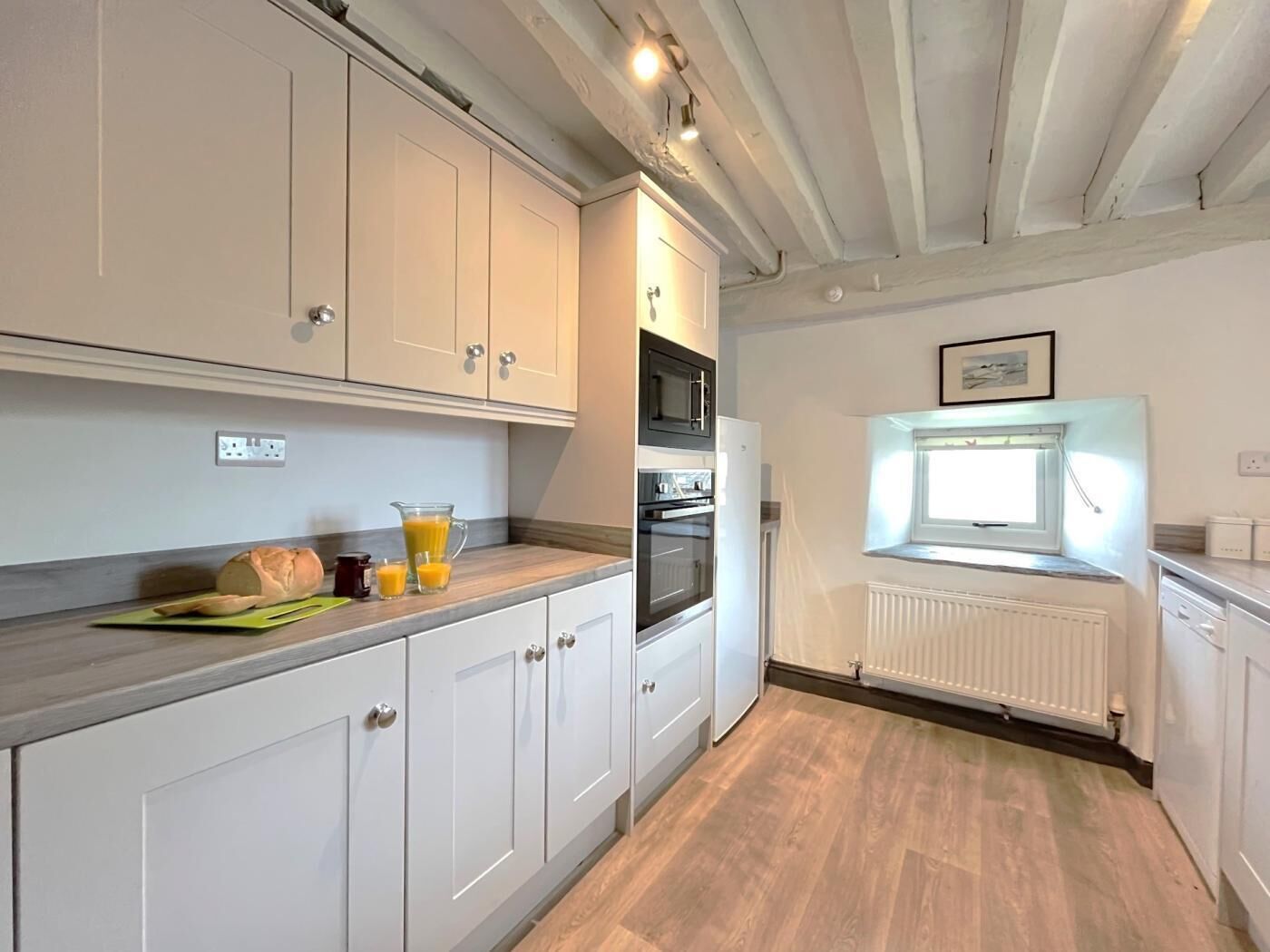 A kitchen with white cabinets, a wooden countertop, a window with a view, and a radiator.