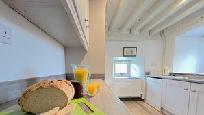 Une cuisine avec une miche de pain, une planche à découper, une carafe de jus d’orange et une fenêtre.