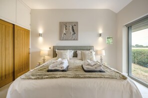A bedroom with a large bed, two bedside lamps, a headboard, and a window with a view of a field. - 2 Bed in Diss (oc-51468) (Burgate Little Green)