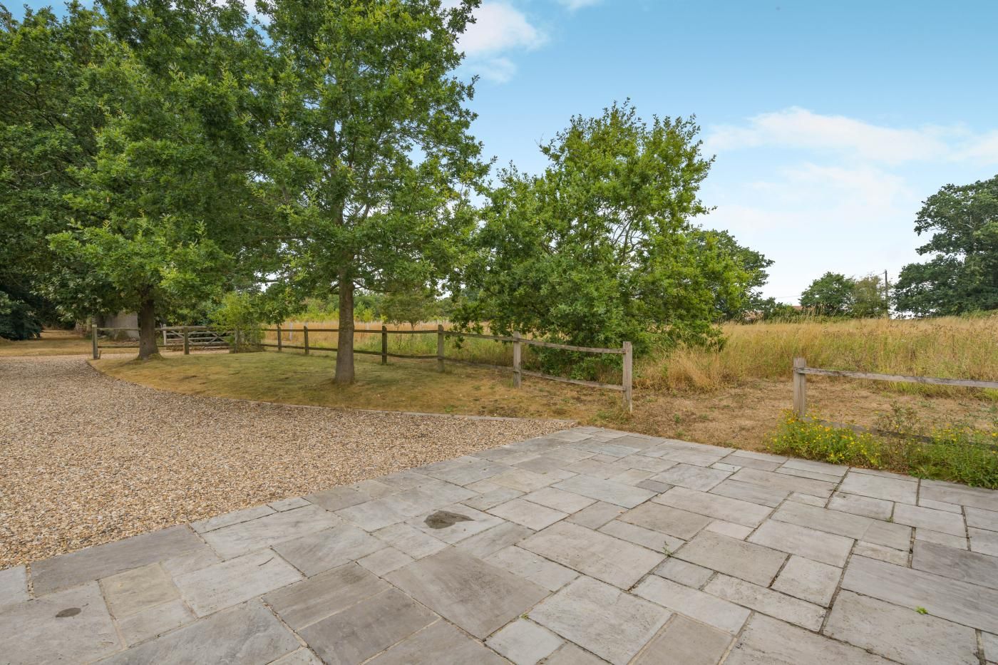 Un espace extérieur aménagé avec un revêtement pavé, un chemin de gravier, une clôture en bois et des arbres.