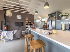 A modern kitchen with a central island, bar stools, a built-in stove, and a large clock on the wall. - 2 Bed in Diss (oc-51468) (Burgate Little Green)