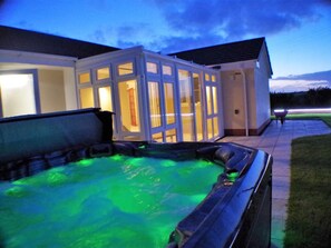 A hot tub with a glass enclosure, a pathway, and a building with a tiled roof. - 3 Bed in Bideford (oc-51790) (Hartland)