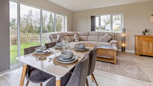 A modern dining area with a table set for four, a sofa, and a cabinet. - 2 Bed in Beaworthy (oc-52087) (Virginstowe)
