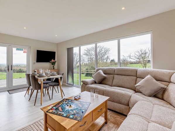 A spacious living room with a large sofa, a dining table, and a board game. - 2 Bed in Beaworthy (oc-52087) (Virginstowe)