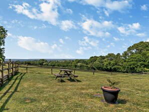 A picnic table in a grassy field with a wooden fence and a potted plant. - 2 Bed in Beaworthy (oc-52087) (Virginstowe)