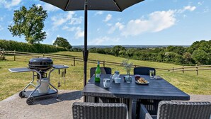 An outdoor patio with a table set for dining, a grill, and a view of the countryside. - 2 Bed in Beaworthy (oc-52087) (Virginstowe)