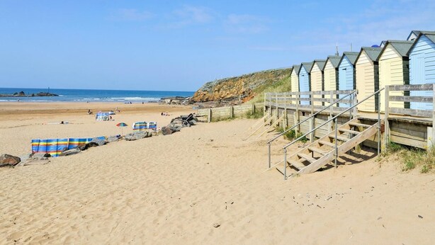 A beach with wooden walkways leading to beach huts, a sandy beach, and the ocean in the background. - 2 Bed in Beaworthy (oc-52087) (Virginstowe)