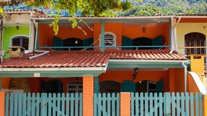 A two-story building with a red-tiled roof, a blue picket fence, and a green and orange facade. - Family home in Lagoinha: sea view, barbecue and 24-hour security. (Ubatuba)