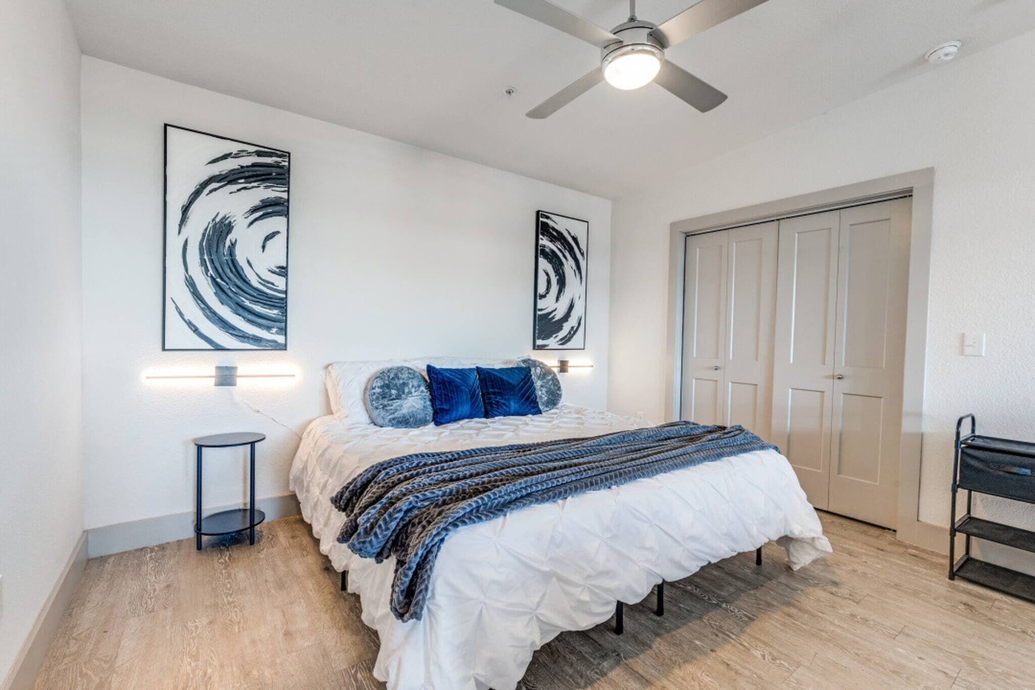 A bedroom with a bed, a ceiling fan, and two wall-mounted light fixtures.