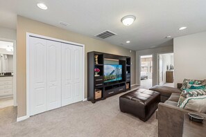 A living room with a flat-screen TV, a brown leather couch, and a white closet. - Sleeps 10*Private Pool*Clubhouse Amenities (Kissimmee)