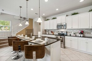 A modern kitchen with white cabinets, a central island, stainless steel appliances, and a dining area with wooden chairs. - Sleeps 10*Private Pool*Clubhouse Amenities (Kissimmee)