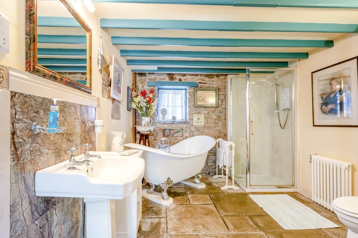 A bathroom with a clawfoot bathtub, a white sink, a shower, and a marble wall.