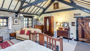 A rustic room with exposed beams, a stone wall, a wooden bed, a sofa, and a large mirror. - 1 Bed in Bude (oc-51546) (Gooseham)