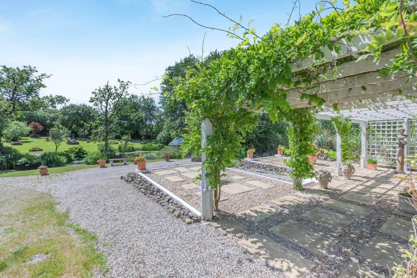 A garden with a pergola, gravel paths, and potted plants.