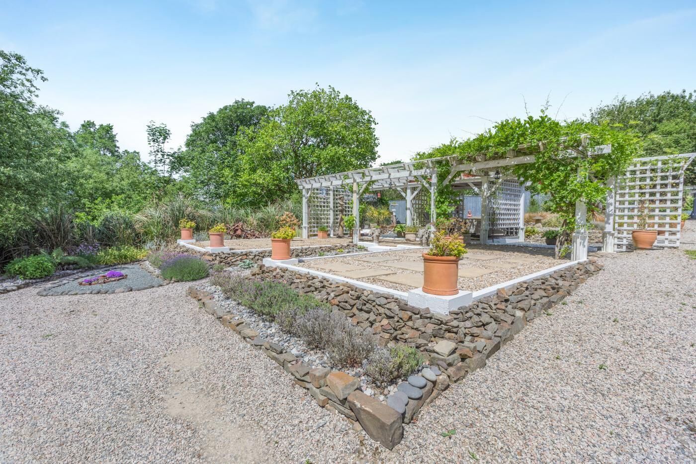 A garden with a pergola, potted plants, and a gravel pathway.