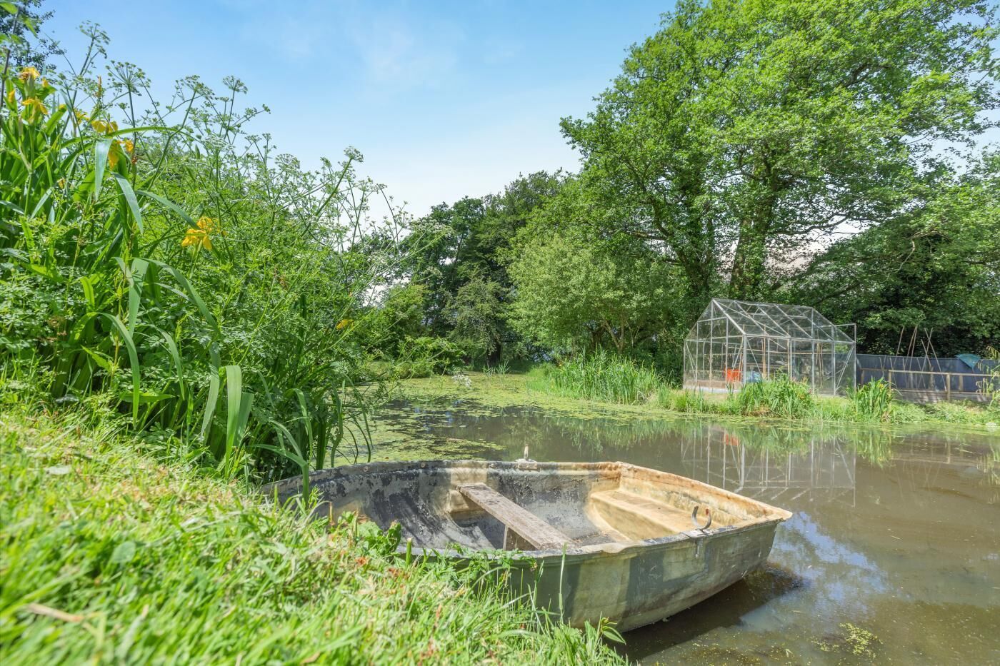 Ein Boot auf einem Teich, umgeben von üppiger Vegetation und einem Gewächshaus.