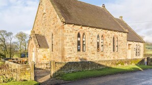 Une église en pierre, dotée d’un toit à forte pente, de fenêtres en arc de cercle et d’un mur en pierre percé d’une porte.