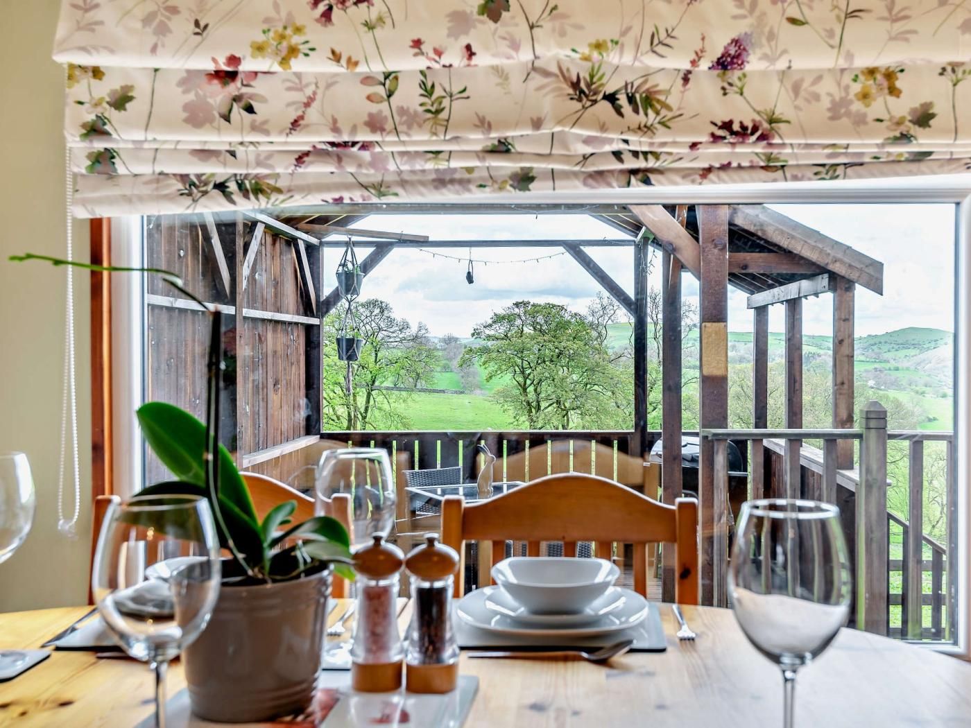 A dining table set for two with a view of a green landscape through a wooden pergola.