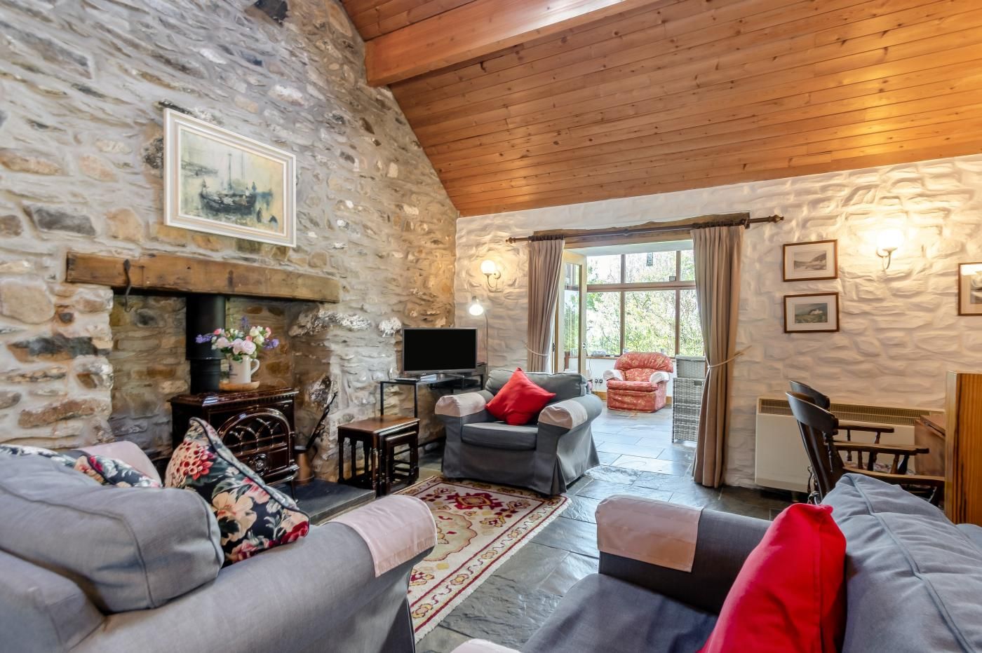A cozy living room with stone walls, a fireplace, a television, and comfortable seating.