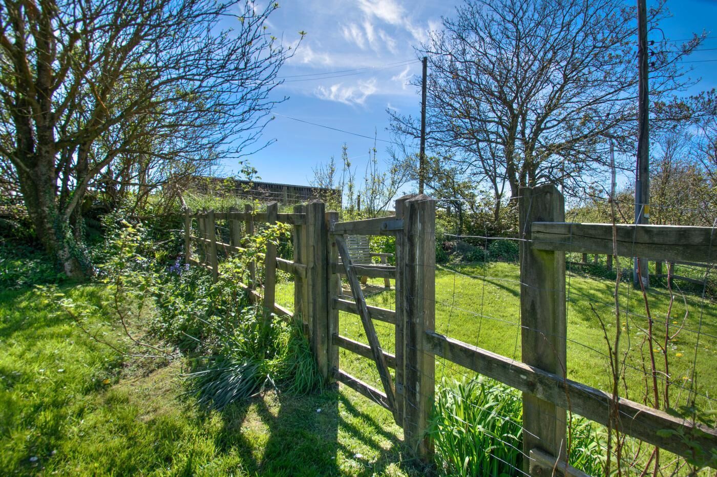 A wooden gate leading to a grassy area with trees and a clear sky.