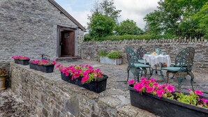 A stone building with a door, outdoor seating with a table and chairs, and flower planters. - 2 Bed in Presteigne (oc-chl34) (Kinnerton)