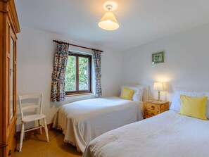 Ein Schlafzimmer mit zwei Betten, einem Sessel, einem Fenster mit Vorhängen, einem Nachttisch mit Lampe und einem Bild an der Wand.