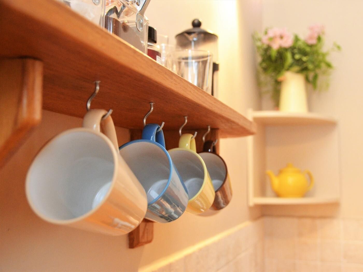 A kitchen with a wooden shelf holding mugs and a yellow teapot.