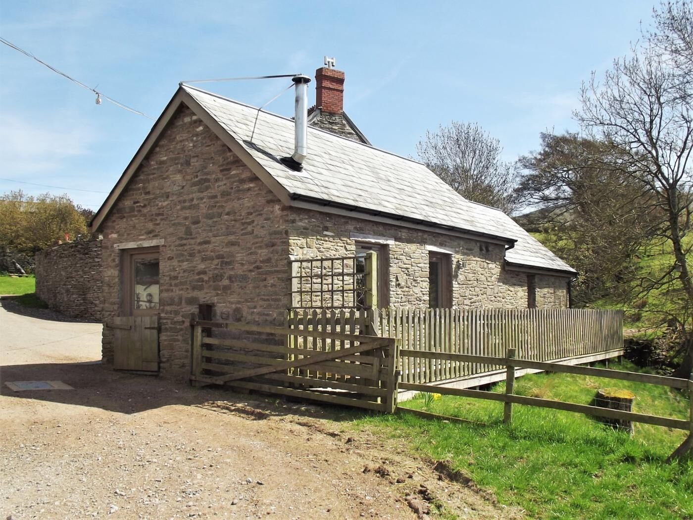 A stone building with a sloped roof, a chimney, and a wooden gate.