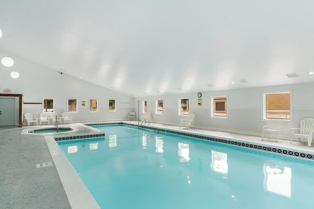 A large indoor swimming pool with clear water, surrounded by white walls and windows.