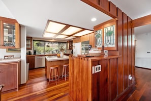 Una cocina moderna con armarios de madera, una isla central con taburetes y un amplio ventanal que proporciona luz natural.