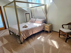A four-poster bed with a wooden frame, a bedside table with a lamp, and a chair.