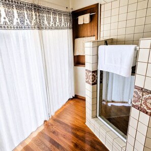 Ein Badezimmer mit Holzboden, einer Duschkabine aus Glas und einer gefliesten Wand mit einem dekorativen Fries.