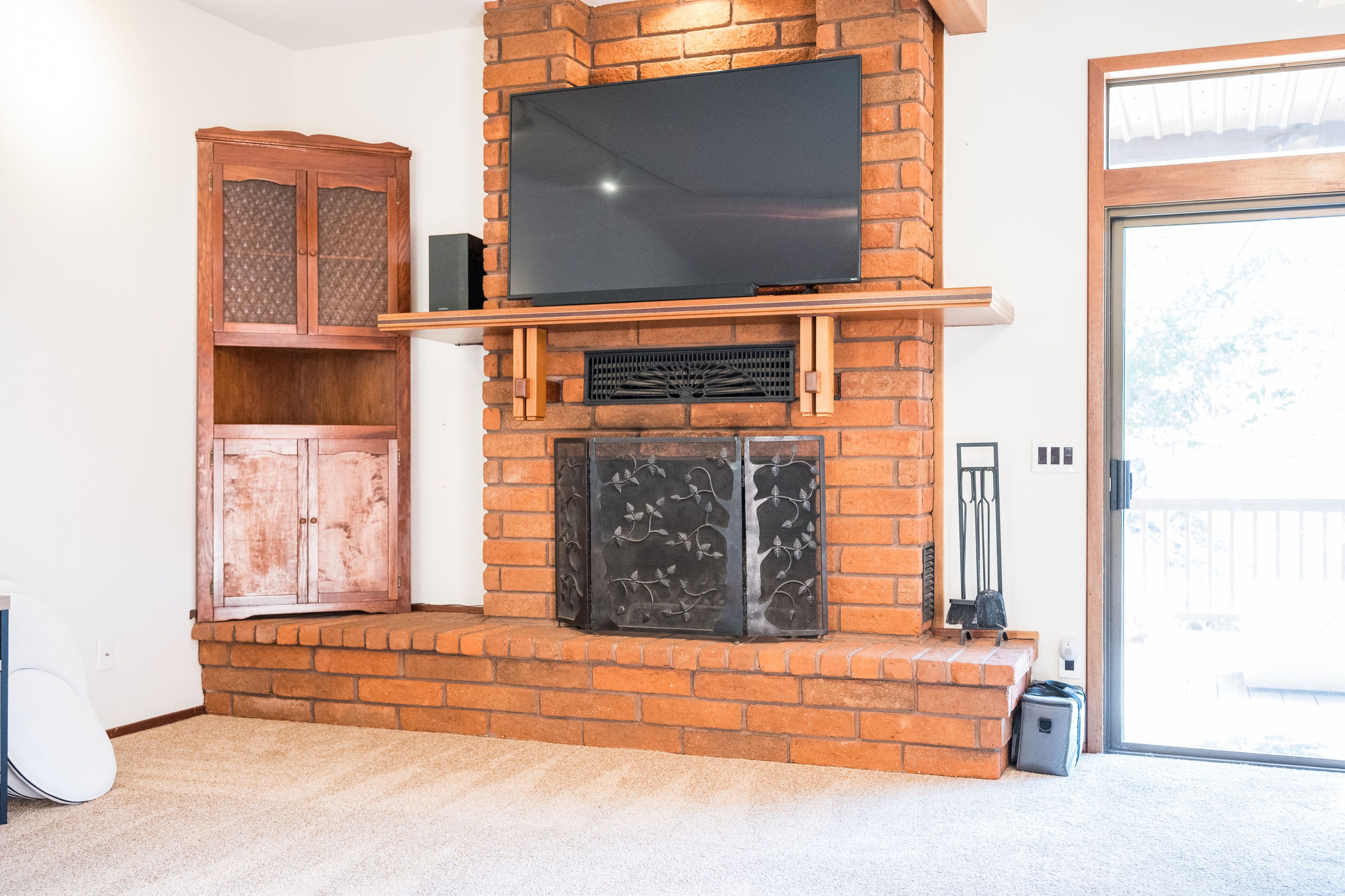 Een woonkamer met een open haard van baksteen, een flatscreen-tv erboven en een houten kast aan de linkerkant.