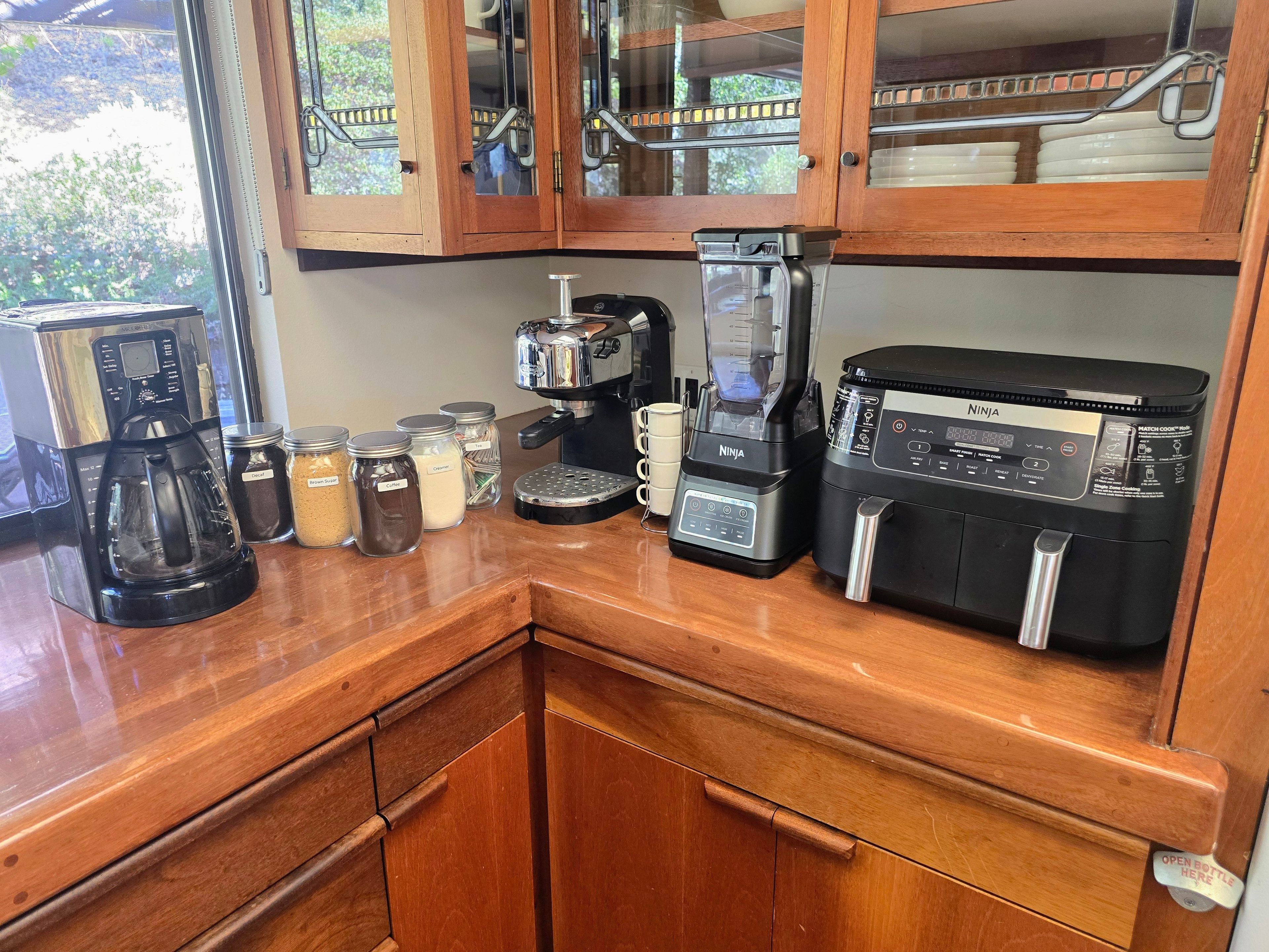 Eine Küchenarbeitsplatte mit Kaffeemaschine, Mixer und Zuckerdosen sowie Sahnejournalen.