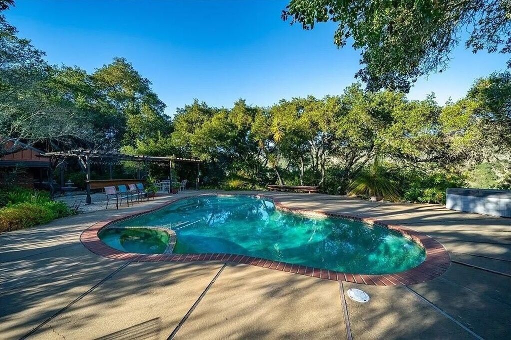 Une piscine bordée de briques, entourée d’une terrasse aménagée avec des chaises longues et une pergola.