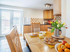 Ein Essbereich mit einem für das Frühstück gedeckten Tisch, einem Kühlschrank und Blick durch die Glastür.