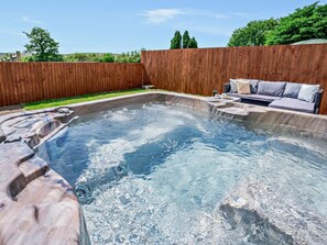 Ein Whirlpool mit einer Holzterrasse und einer Sitzecke mit Kissen.